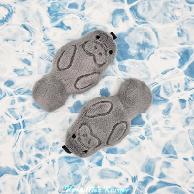 Two plush manatee keychains on a paper water background